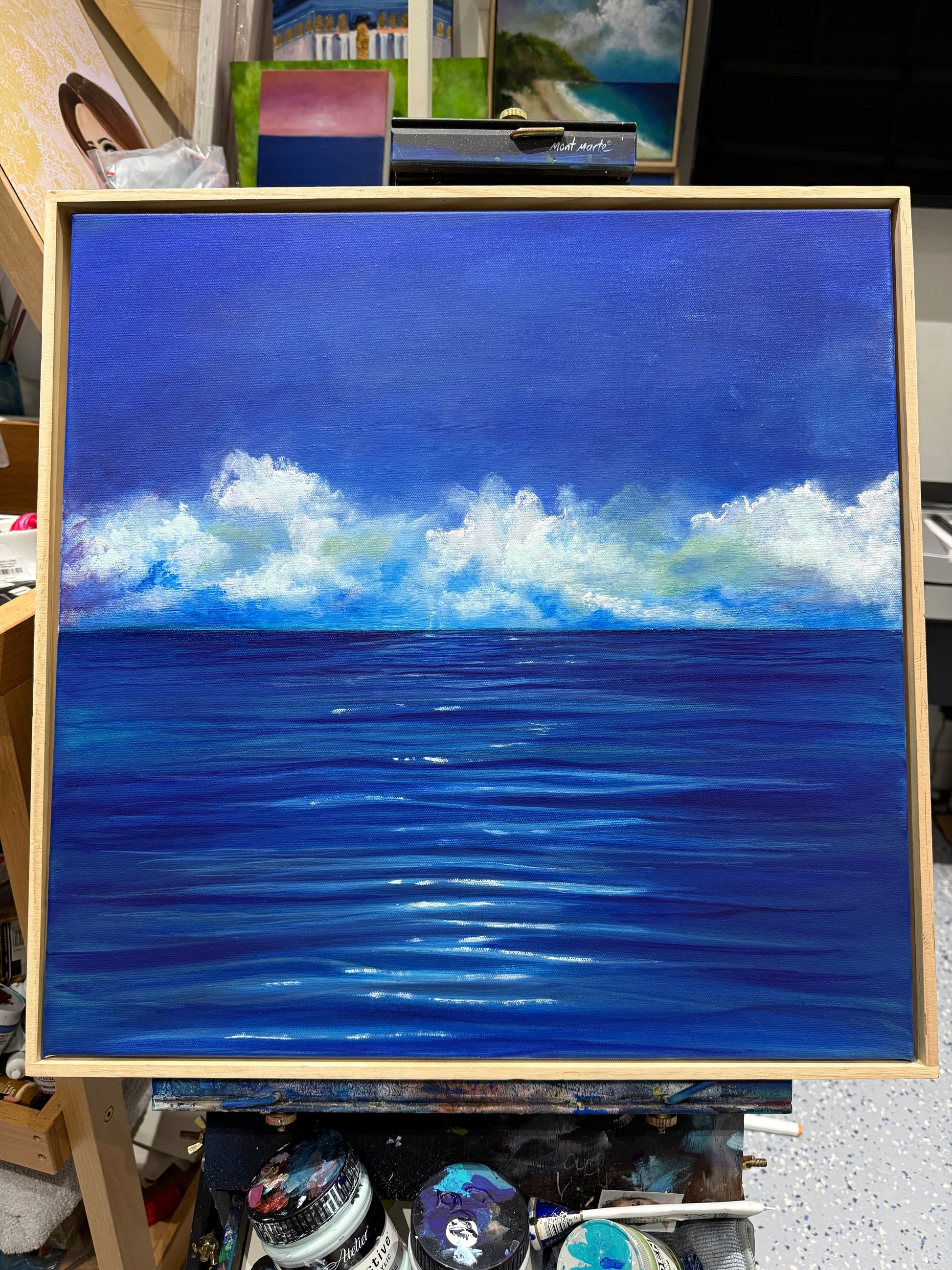 The Weight of Blue by Dallal Naser. Blue ocean with white clouds on an easel.